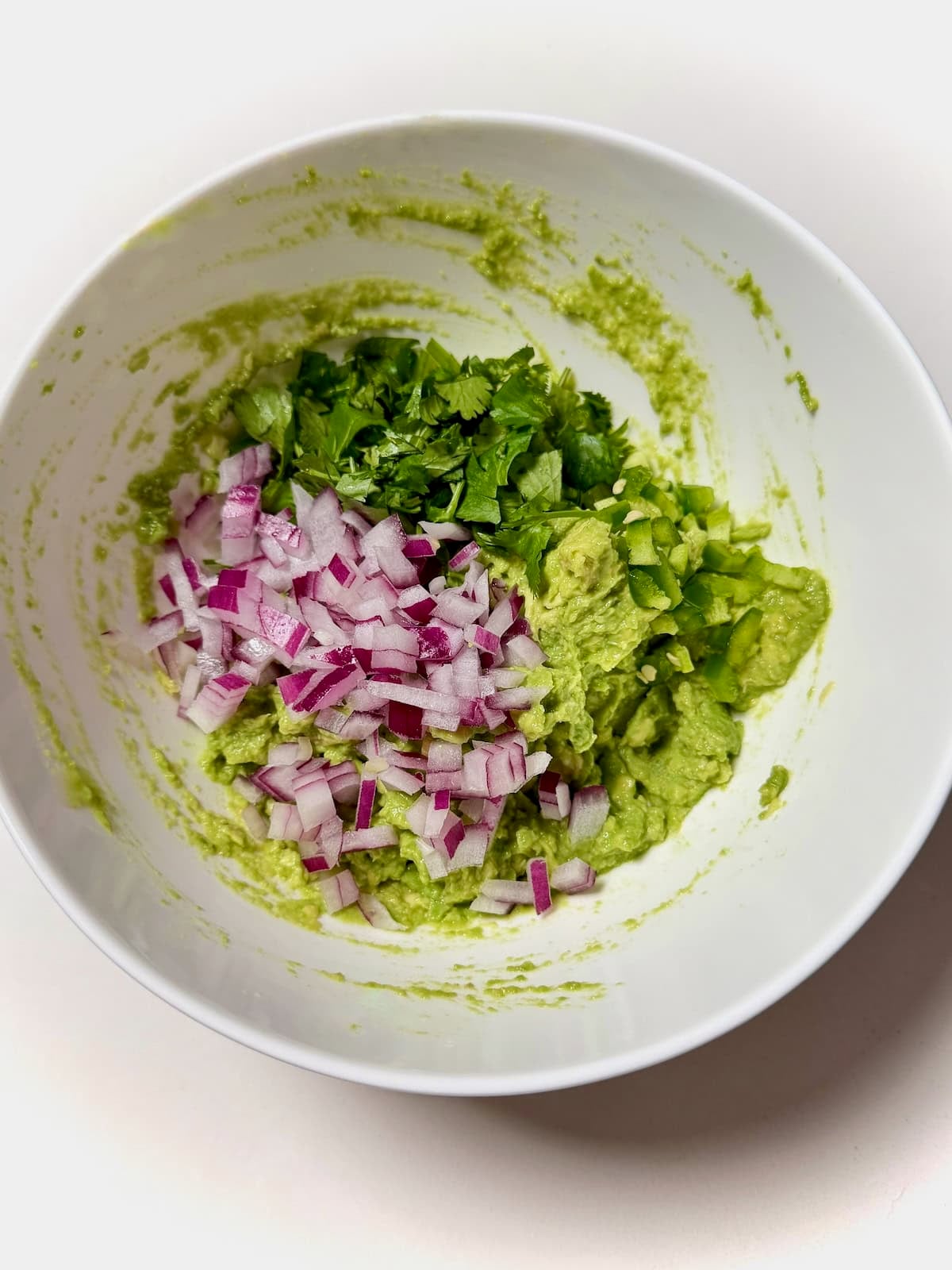 Mashed avocado with chopped red onion, cilantro, and jalapeno in bowl.
