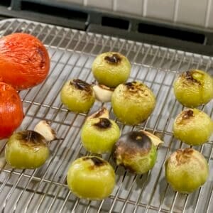 Broiled tomatillos, tomatoes, and garlic on wire rack on baking sheet.