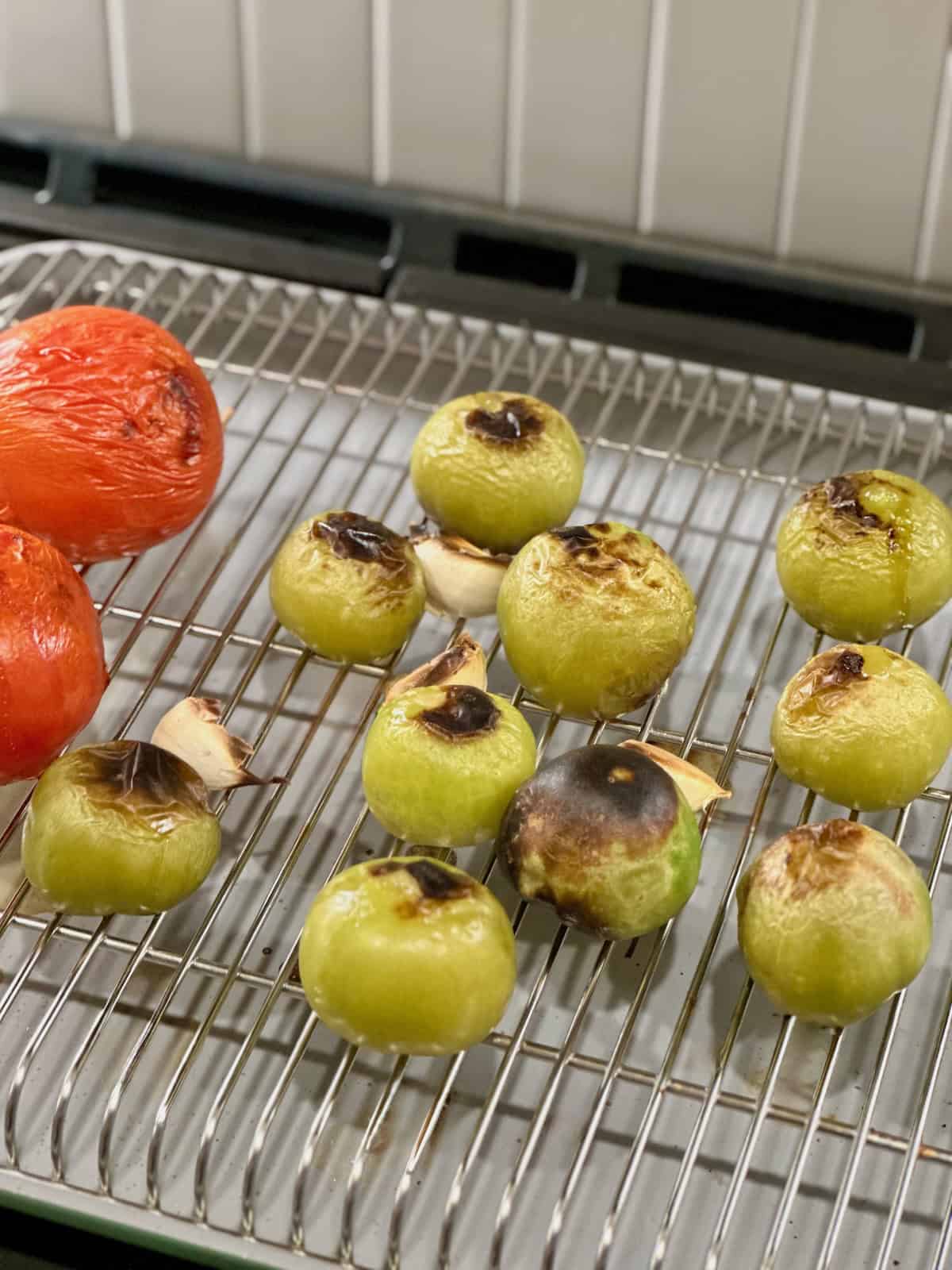 Broiled tomatillos, tomatoes, and garlic on wire rack on baking sheet.