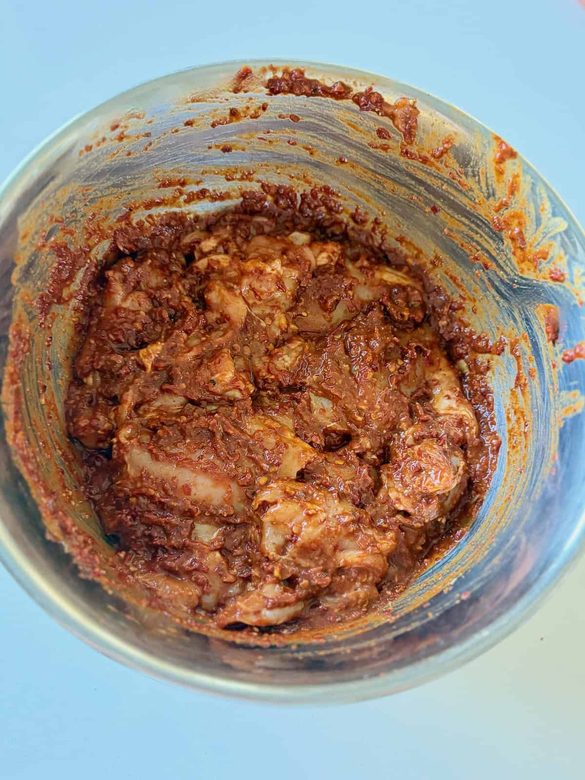 Chipotle chicken marinaded mixed with raw chicken thighs in metal bowl.