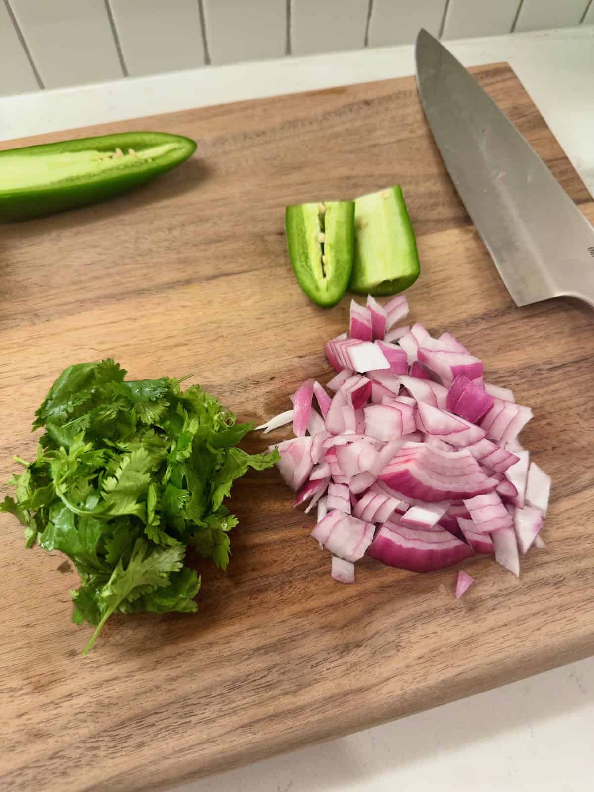Jalapeno, cilantro, and tomatoes chopped on cutting board.
