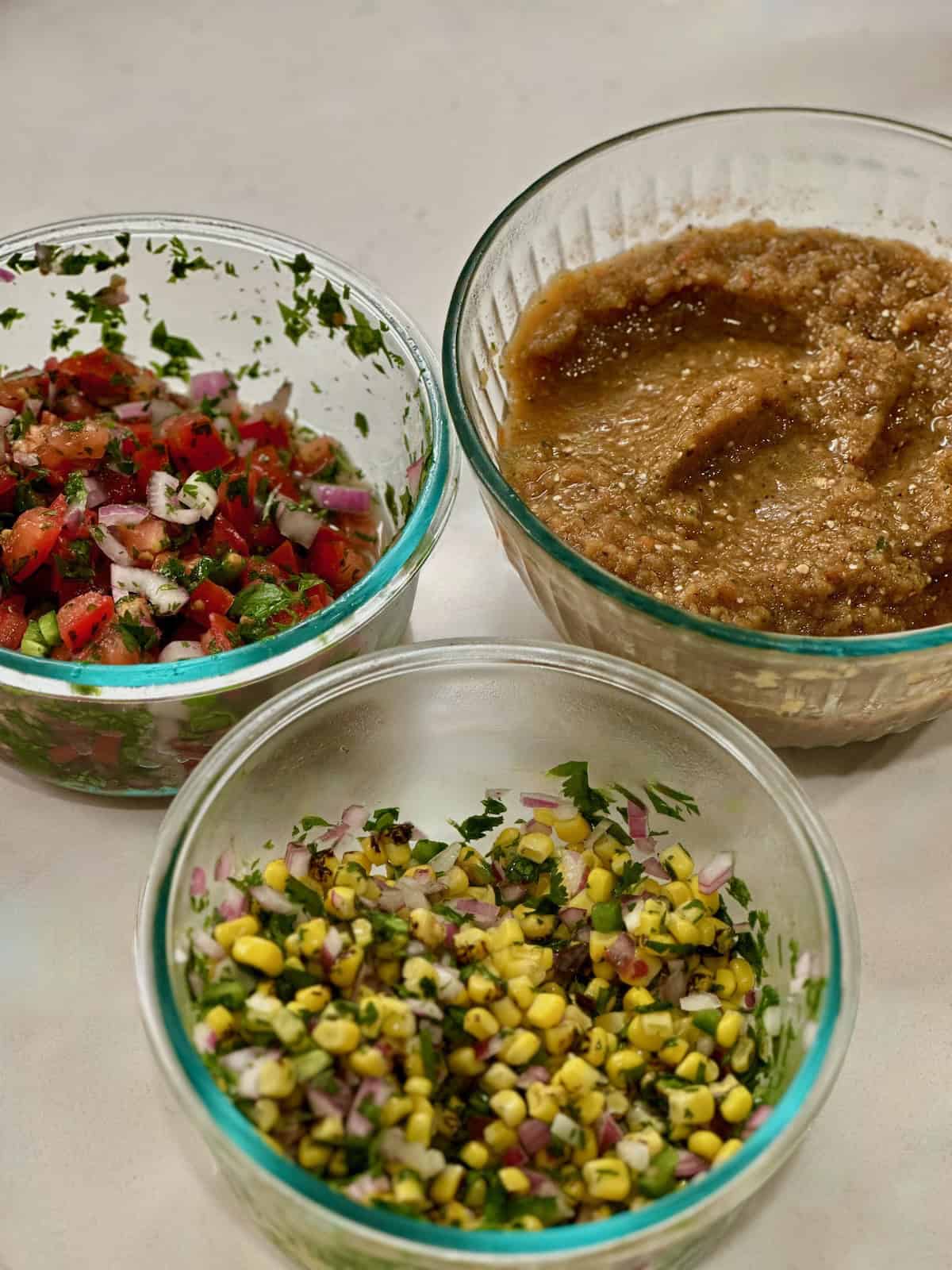Chipotle copycat tomato salsa, corn salsa, and tomatillo salsa in bowls.