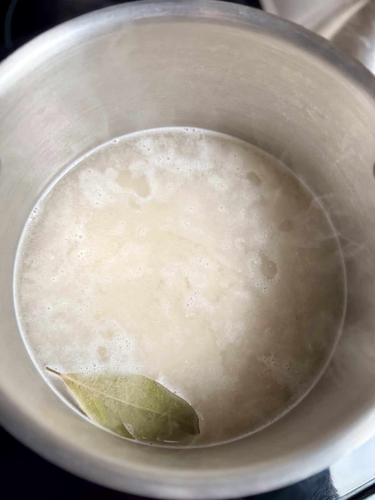 Long grain white rice in a pot with water and bay leaf before cooking cilantro lime rice.