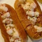 Two butter poached shrimp rolls on a plate with a lemon wedge.