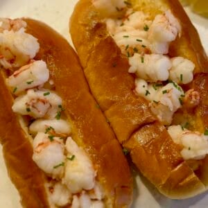 Two butter poached shrimp rolls on a plate with a lemon wedge.