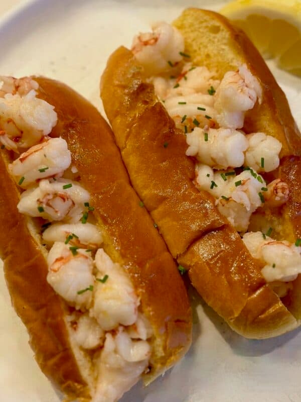 Two butter poached shrimp rolls on a plate with a lemon wedge.