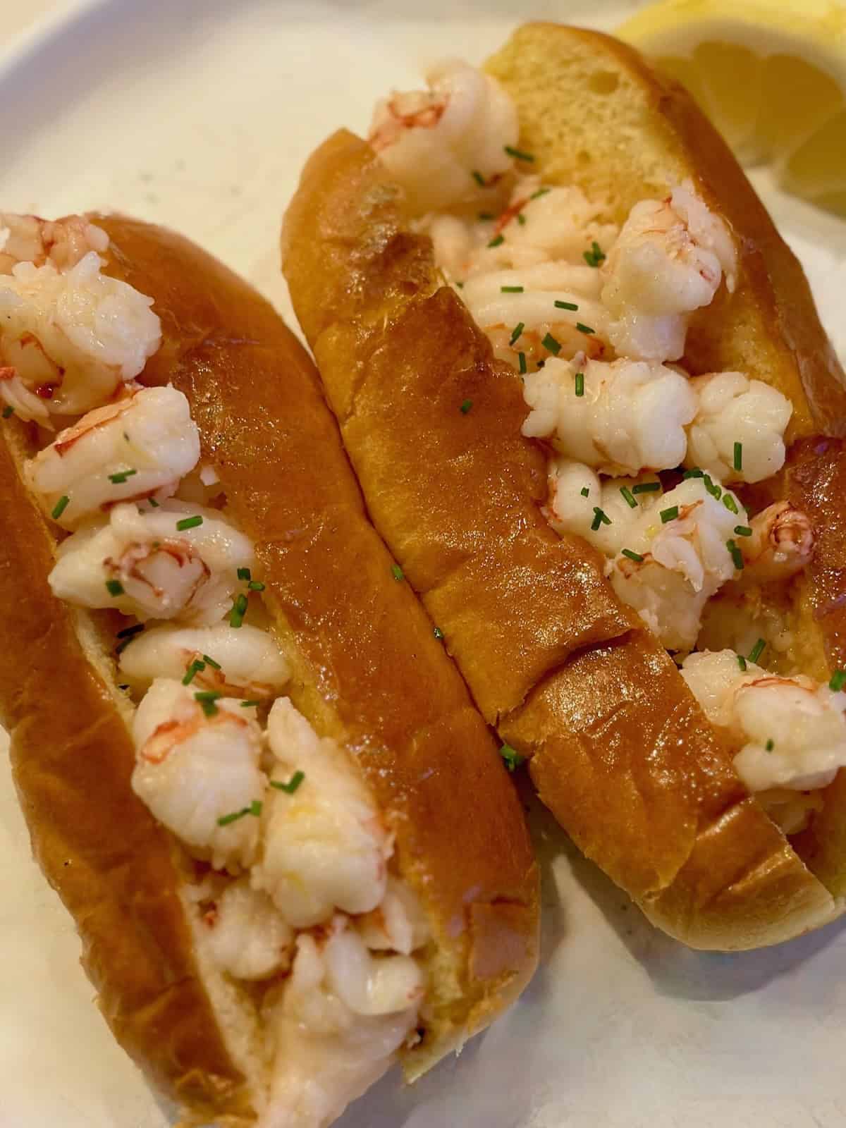Two butter poached shrimp rolls on a plate with a lemon wedge.