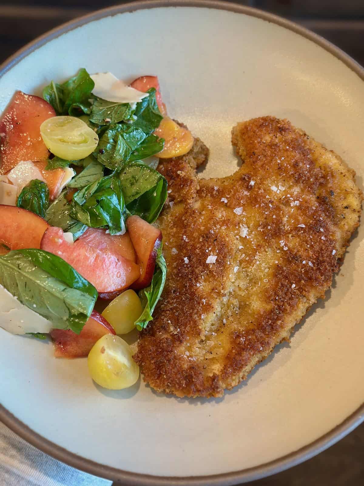 A shallow bowl with crispy chicken milanese and peach and tomato salad