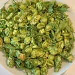 Green pasta salad with chicken in a white serving bowl.