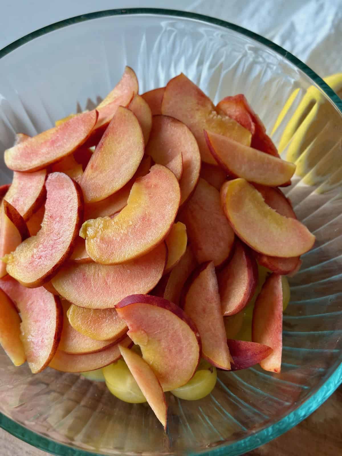A glass bowl with thinly sliced peaches and sliced yellow tomatoes
