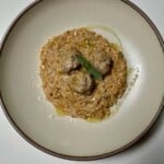 Baked pork sage meatballs over creamy apple cider orzo with a drizzle of olive oil and a sage leaf on plate.