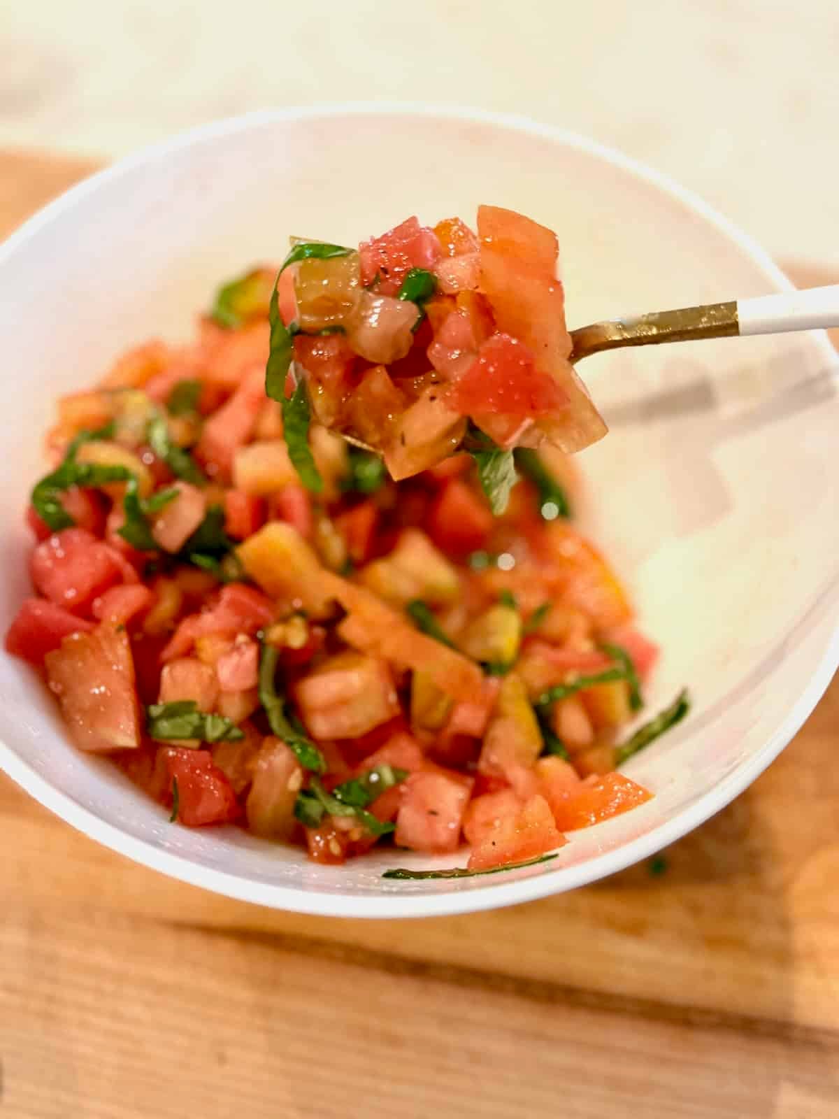 Diced tomatoes, basil, and olive oil combined in a bowl on a spoon for topping.