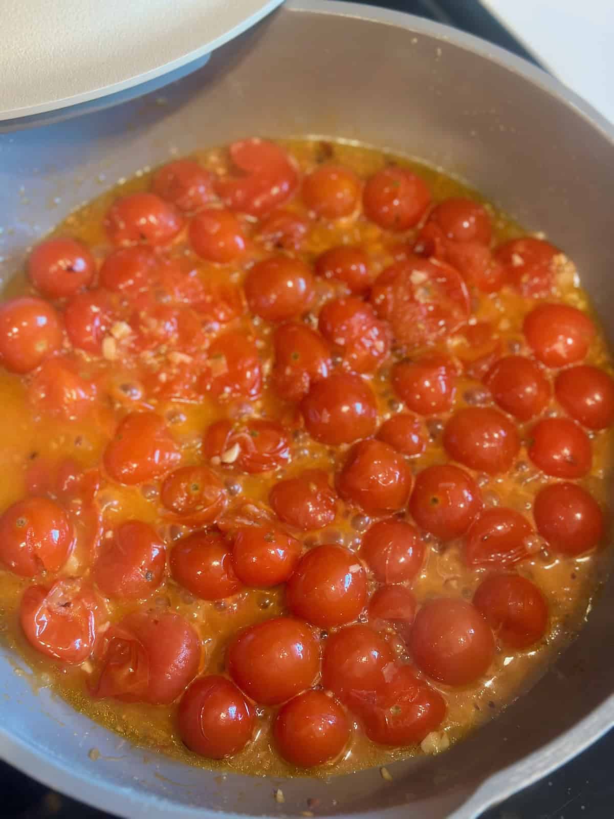 Cherry tomatoes cooking in a skillet after bursting and releasing their juices to create the sauce for Tomato Basil Shrimp Pasta.