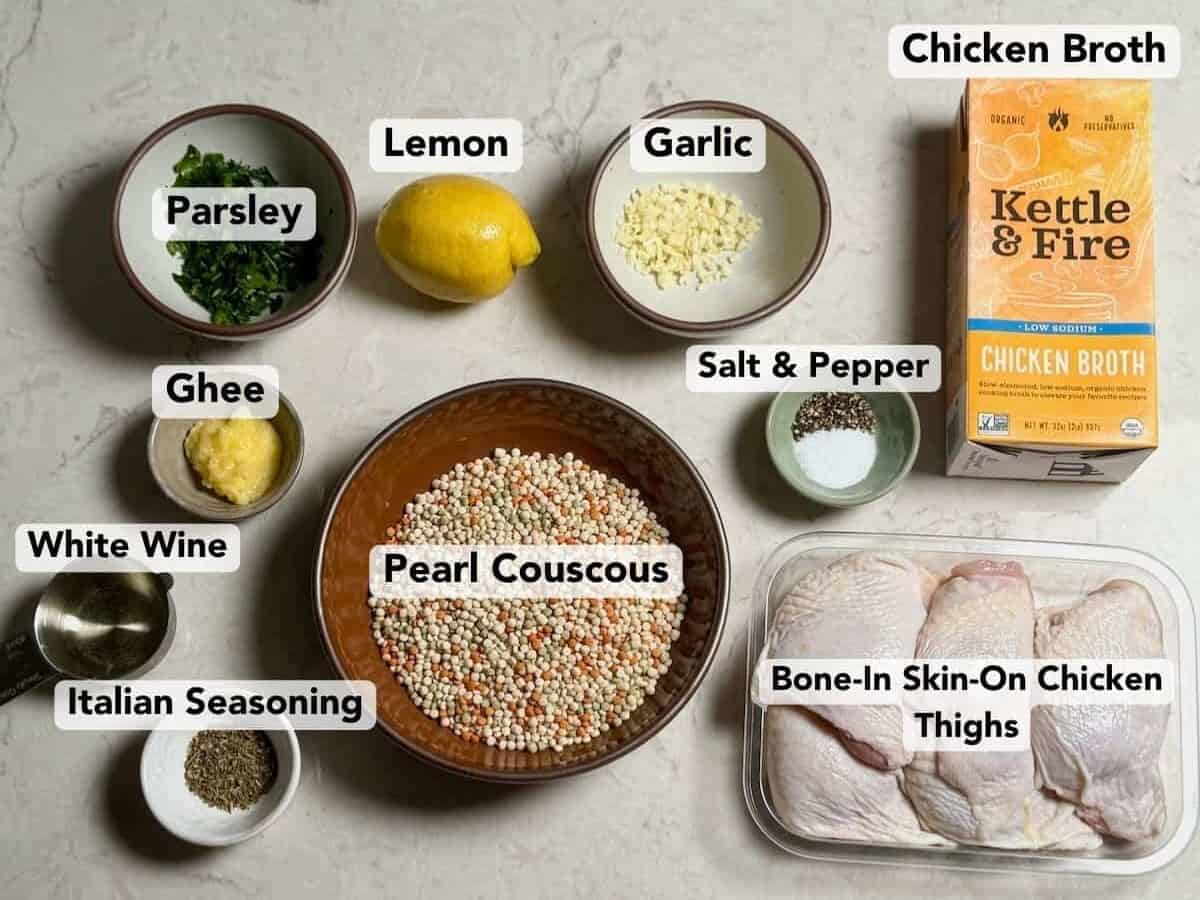 Labeled ingredients for one pan crispy chicken thighs with lemon couscous including chicken thighs, pearl couscous, lemon, garlic, and parsley.