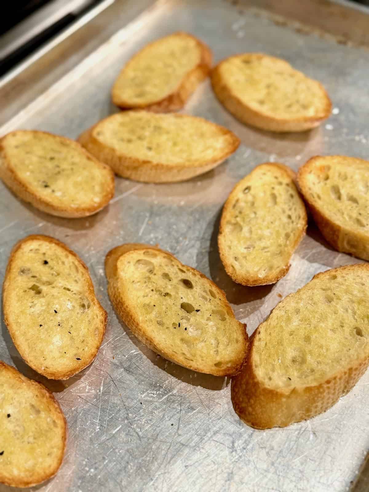 Toasted crostini on a baking sheet for whipped ricotta bruschetta dip.