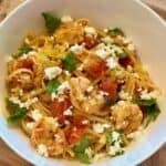 Tomato Basil Shrimp Pasta in a white bowl with lemon zest, basil, and feta cheese.