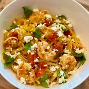 Tomato Basil Shrimp Pasta in a white bowl with lemon zest, basil, and feta cheese.