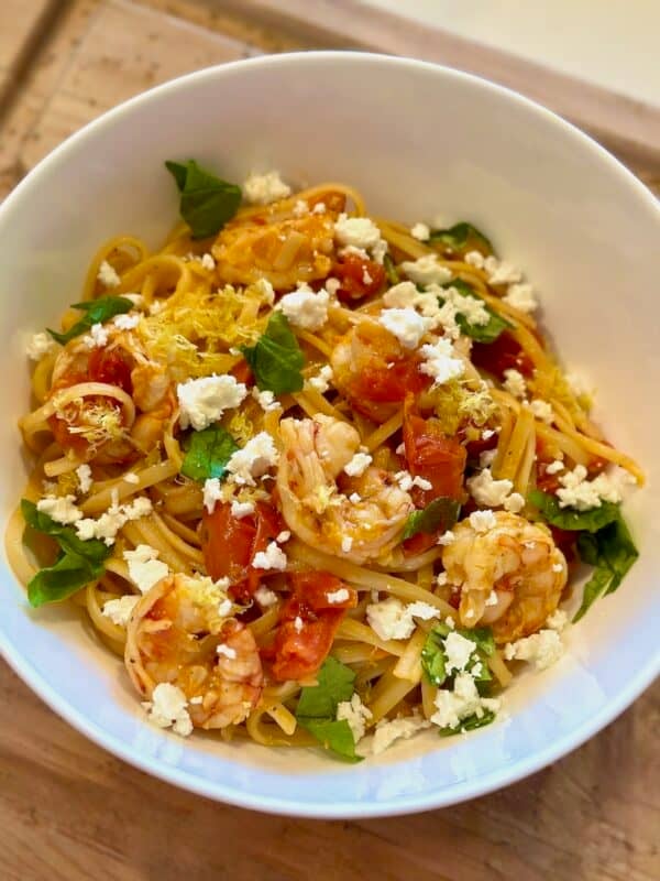 Tomato Basil Shrimp Pasta in a white bowl with lemon zest, basil, and feta cheese.