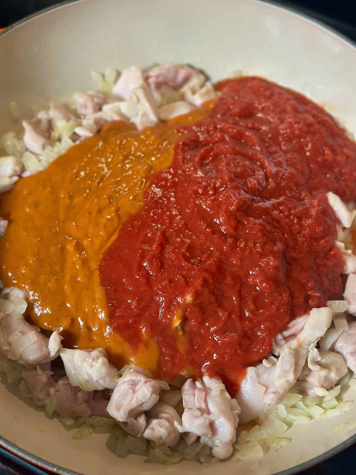Chicken and onions in pan with crushed tomatoes and chicken tikka masala simmer sauce on top.