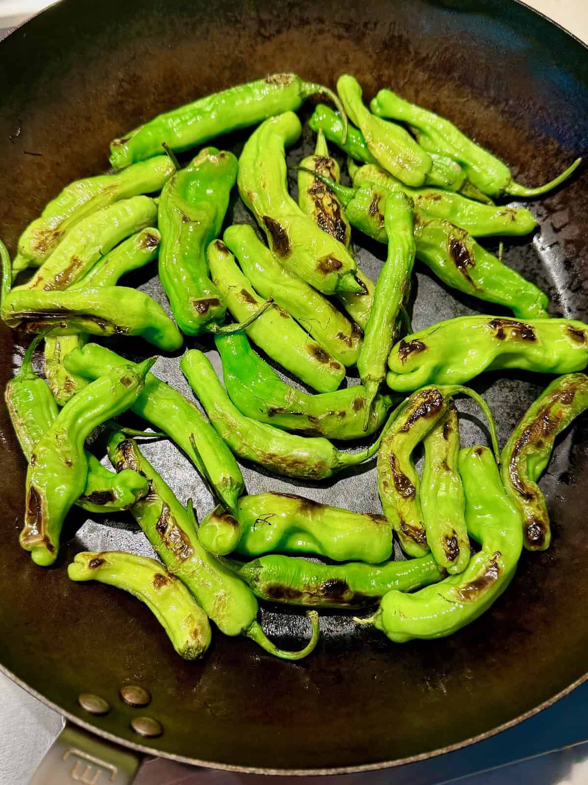 Shishito peppers blistering in a skillet until lightly charred.