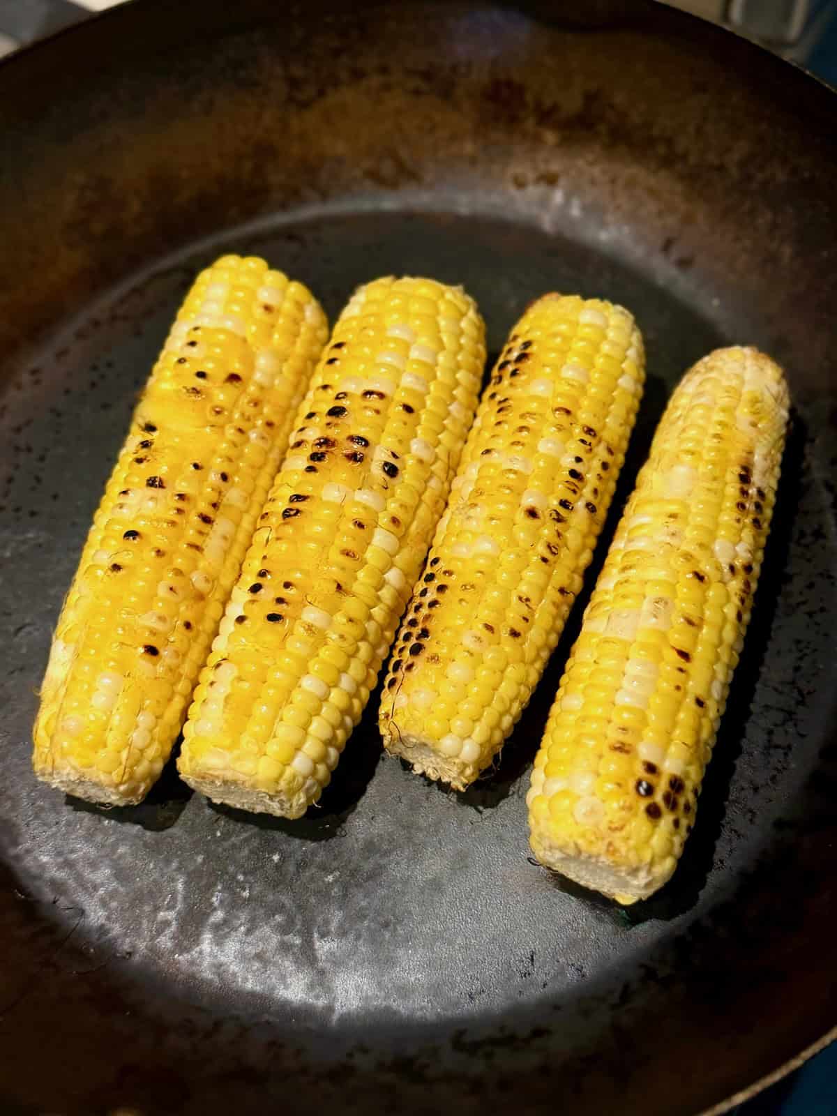 Fresh ears of corn charring in a skillet until lightly blackened.