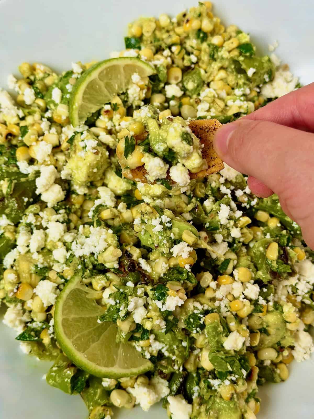 Chip scooping charred corn salad with avocado, shishito peppers, and queso fresco.