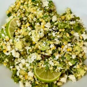 Bowl of charred corn salad with shishito peppers, avocado, queso fresco, cilantro, and lime.