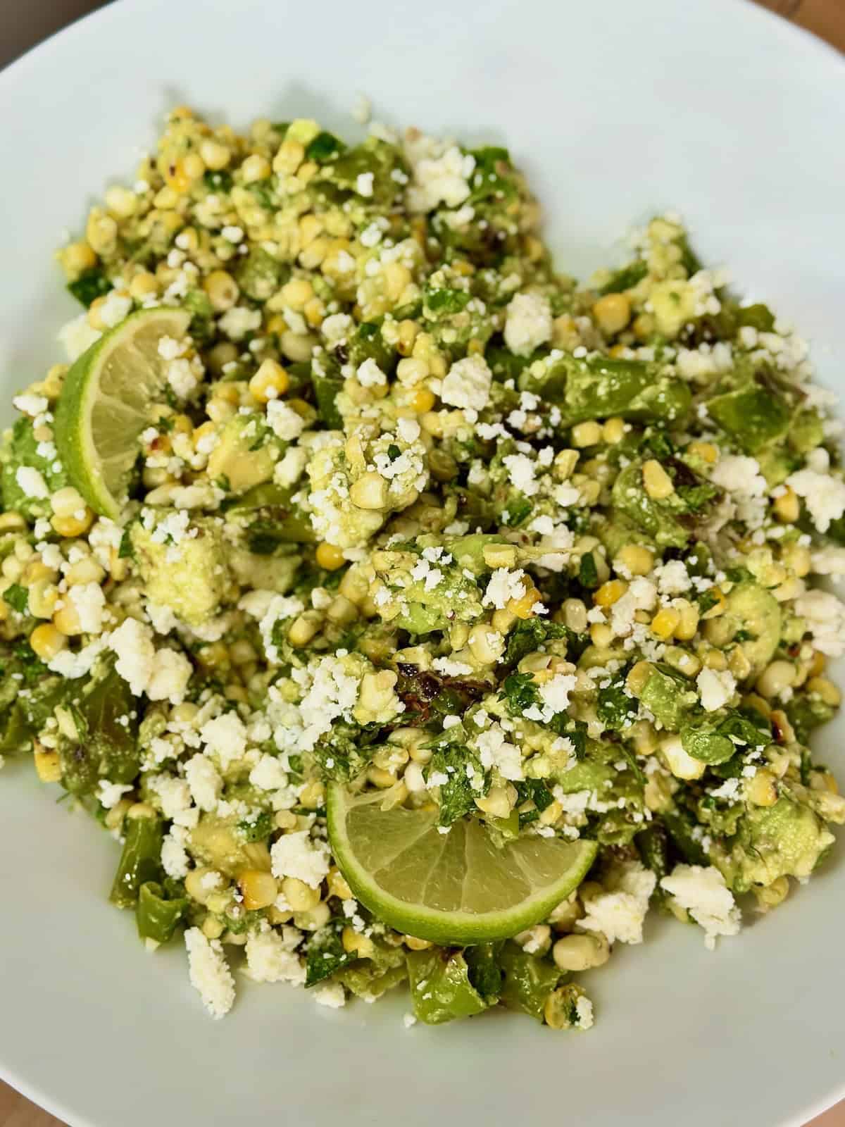 Bowl of charred corn salad with shishito peppers, avocado, queso fresco, cilantro, and lime.