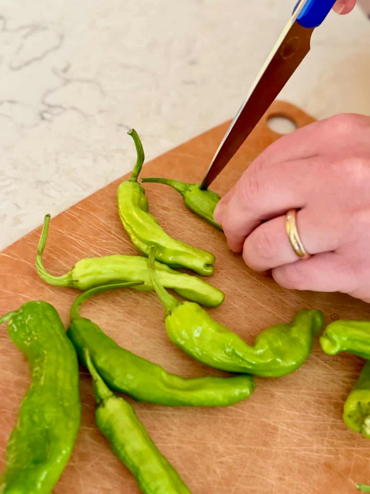 Using a knife to poke small holes in shishito peppers before cooking.