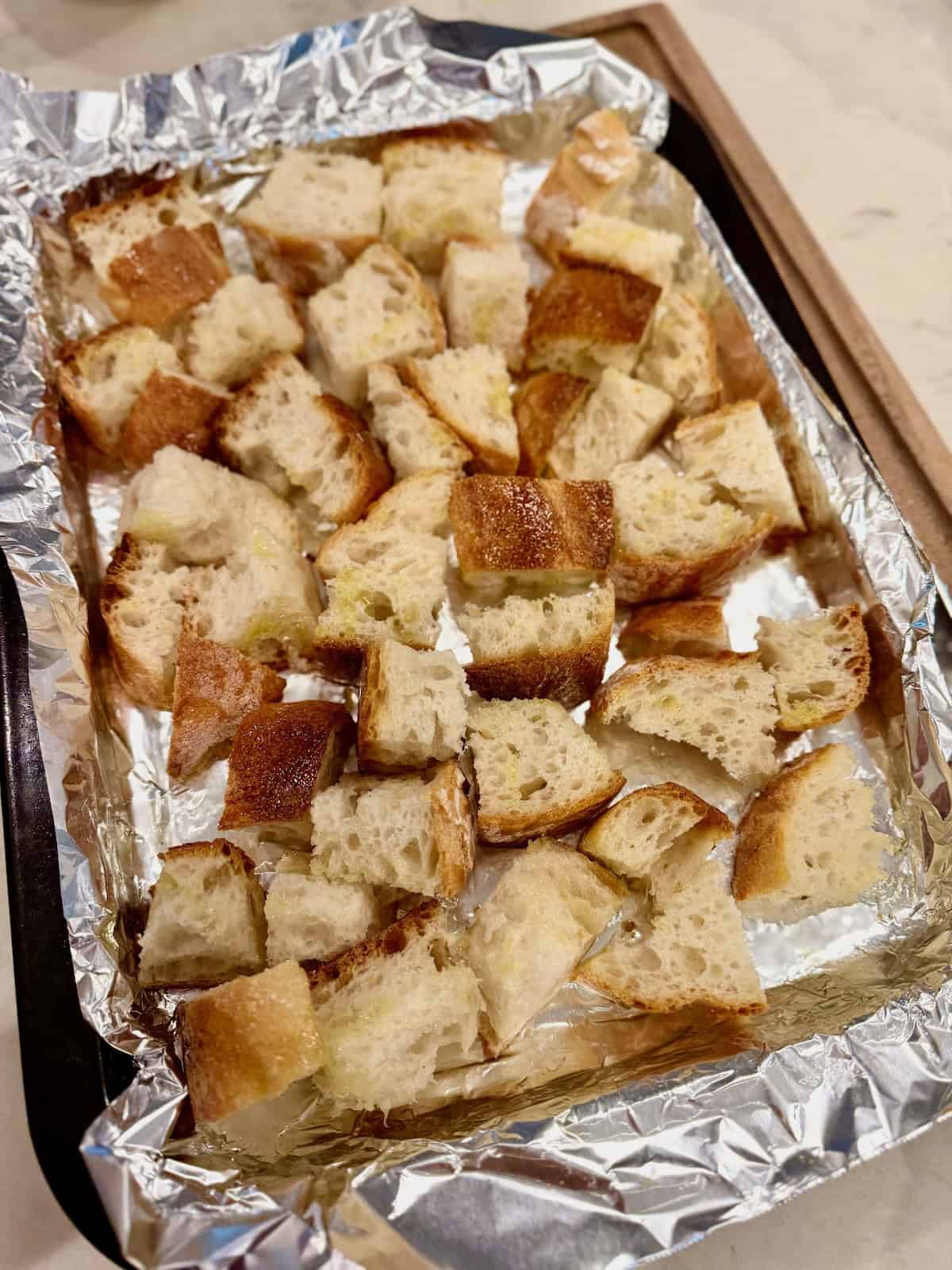 Toasted ciabatta bread cubes on a baking sheet for stone fruit panzanella salad.
