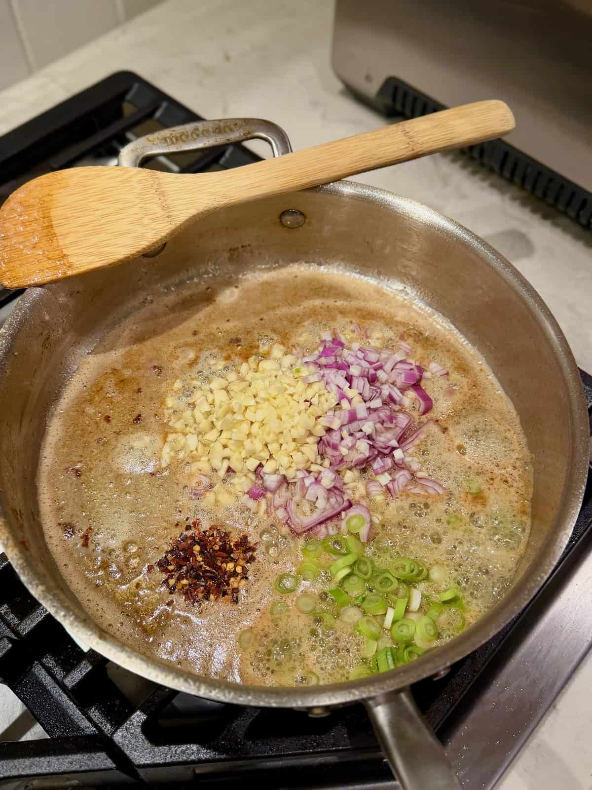 Chopped garlic, shallot, green onion, and red pepper flakes cook in melted butter.