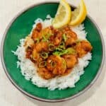 Hawaiian garlic shrimp is served over white rice with green onions and lemon wedges.