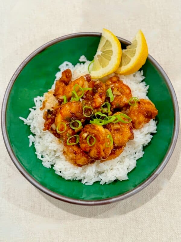 Hawaiian garlic shrimp is served over white rice with green onions and lemon wedges.