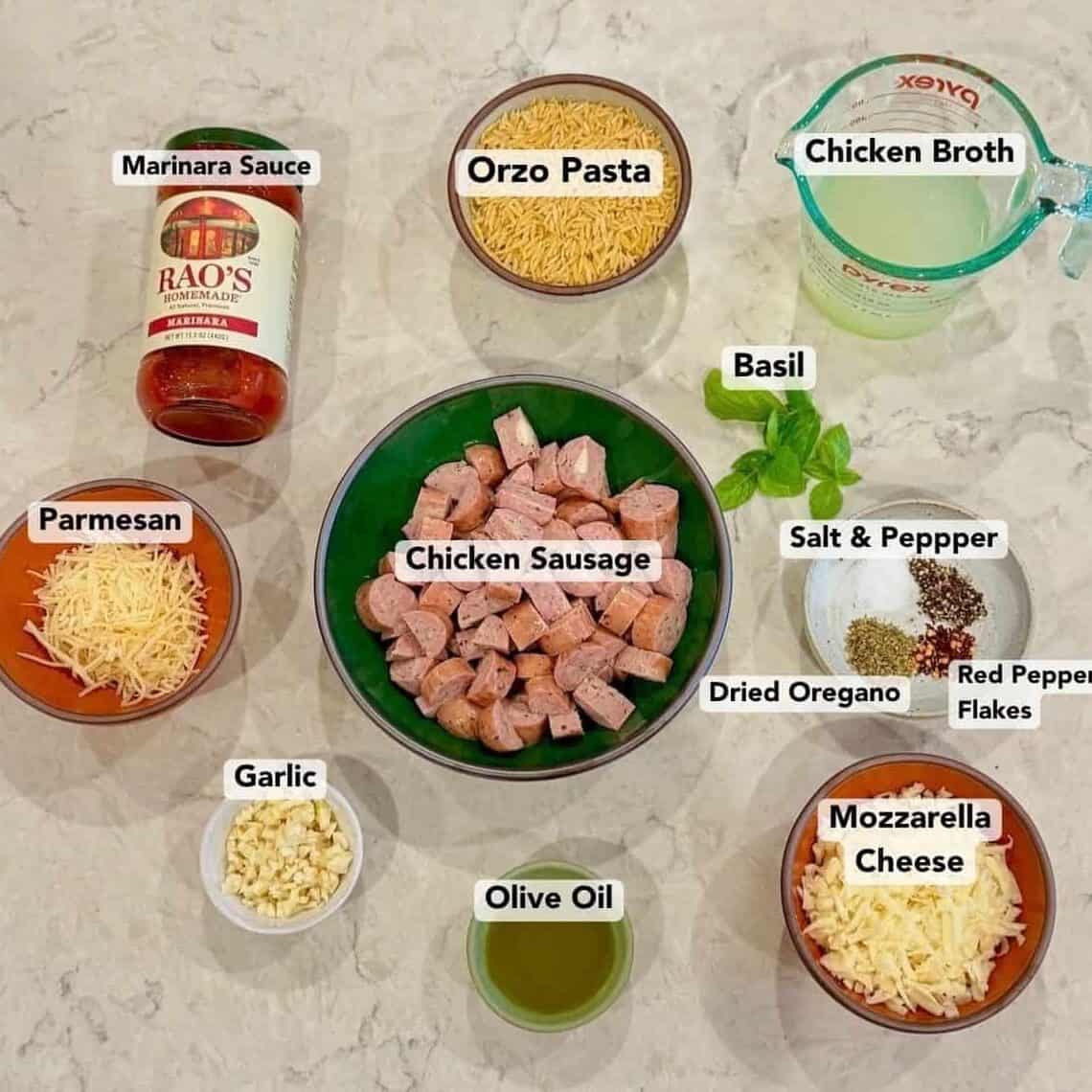 Ingredients for one pan sausage orzo arranged on a light countertop.