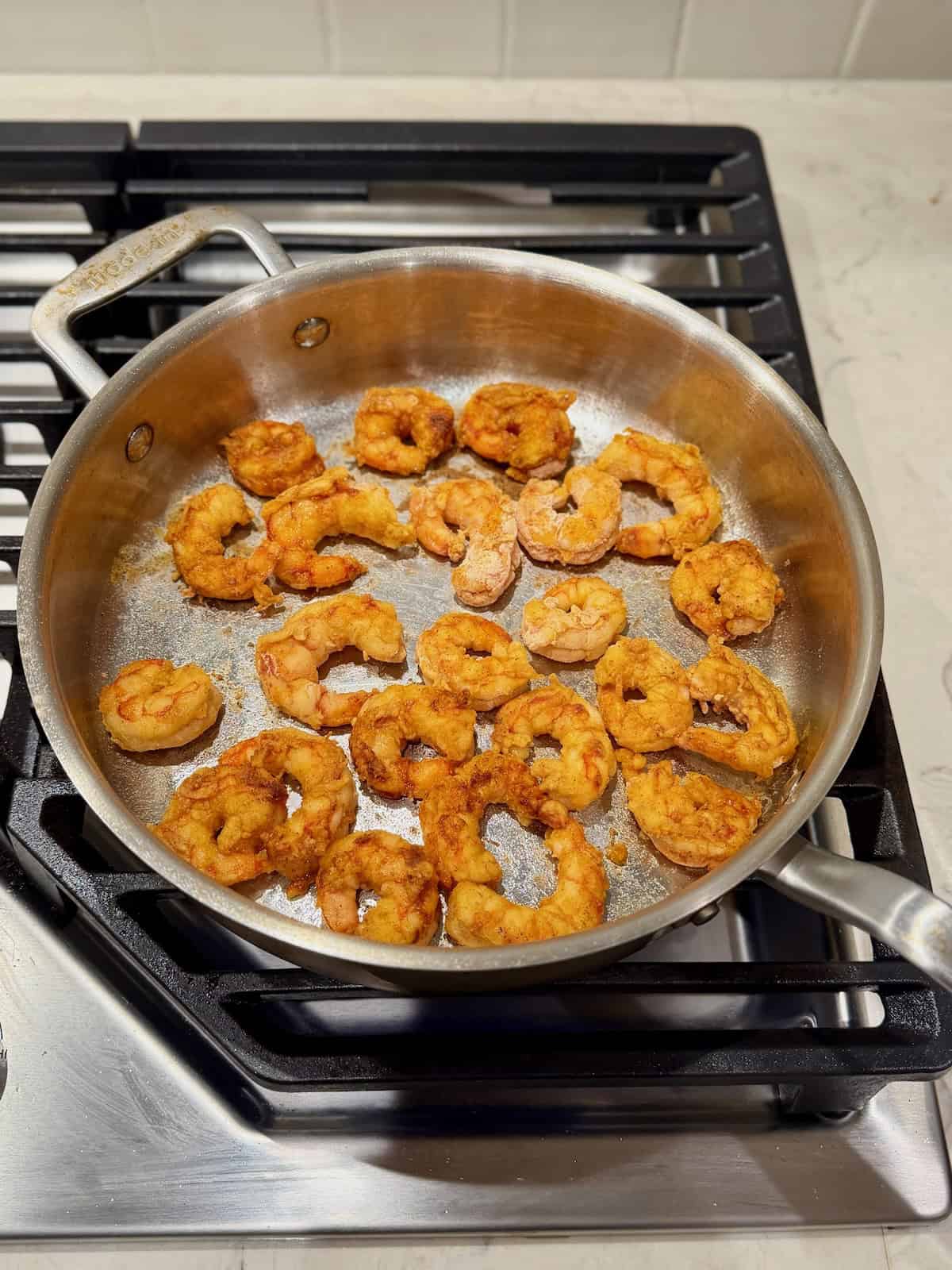 Flour-coated shrimp are browned in a stainless steel pan until golden.