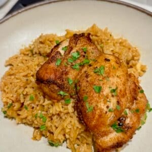 Golden brown chicken thigh rests on seasoned rice with chopped parsley.
