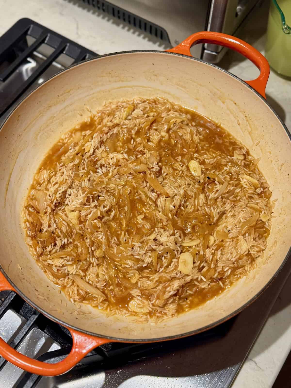 Jasmine rice simmers in apple cider and chicken broth in braiser.