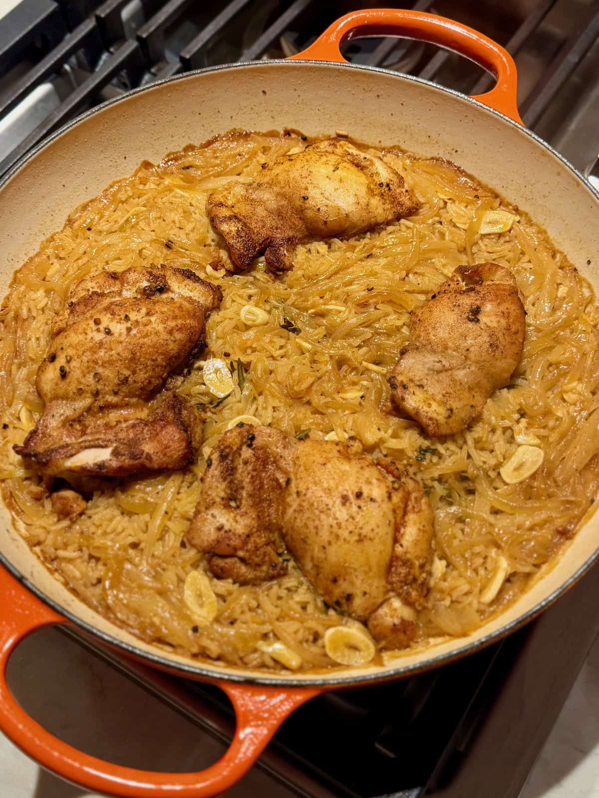 Golden chicken thighs sit over cooked apple cider rice in a braiser.
