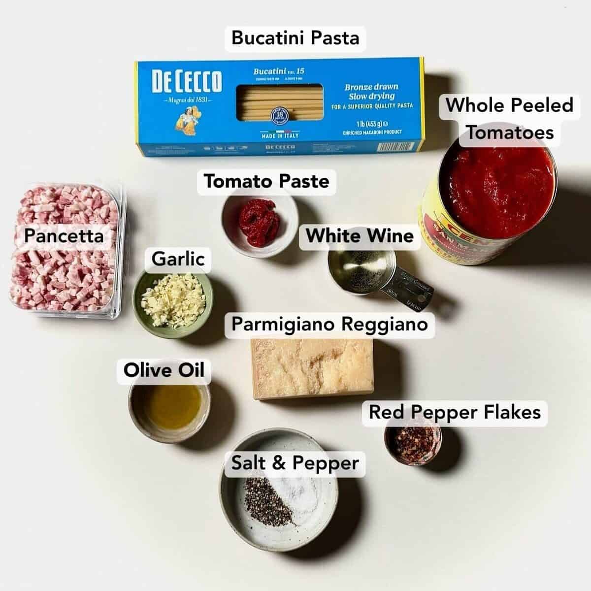 Ingredients for bucatini amatriciana including pancetta, tomatoes, bucatini, garlic, olive oil, and pecorino cheese.