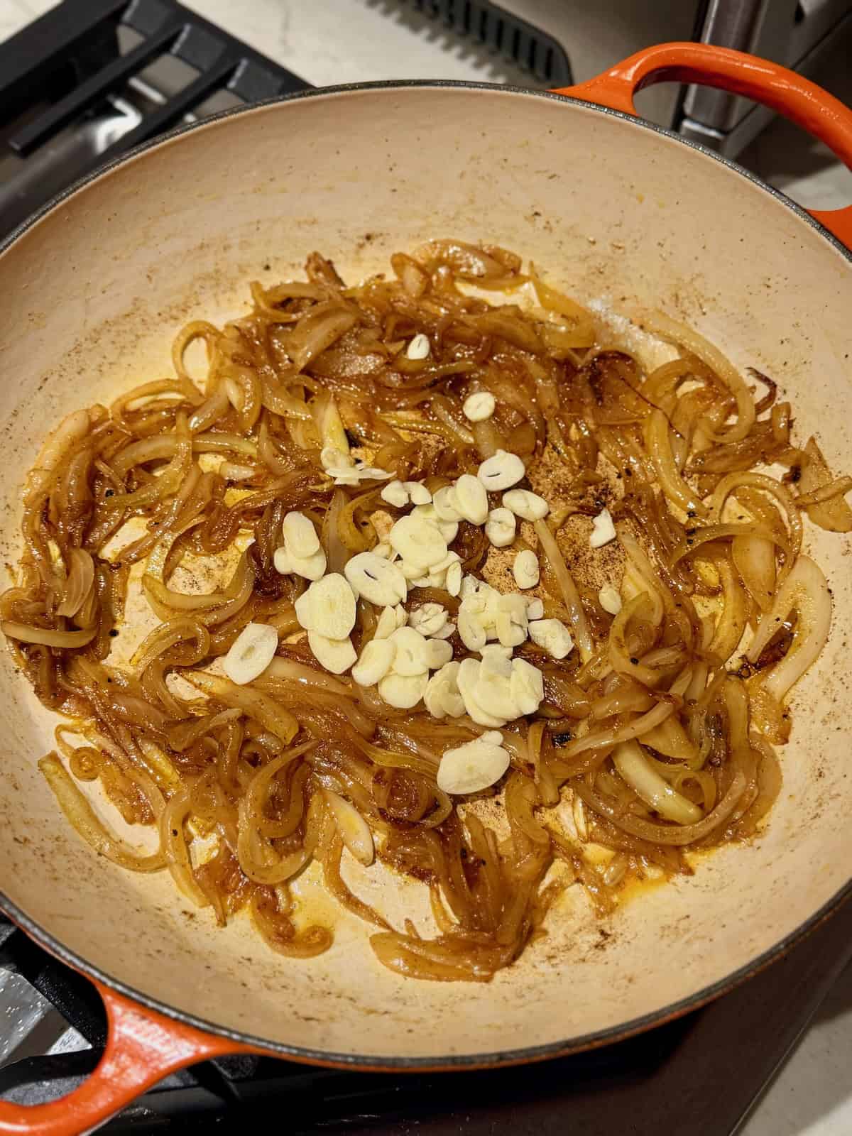 Cooked onions and sliced raw garlic in a braiser.