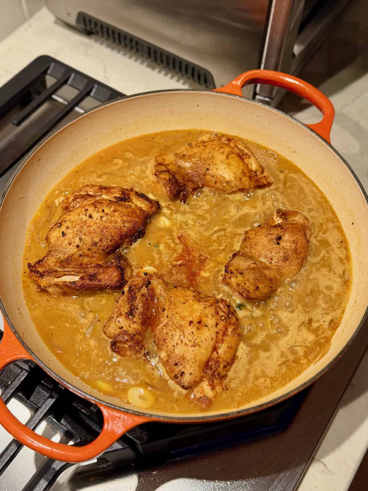 Seared chicken thighs rest over rice and apple cider braising liquid.