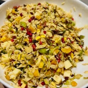 Warm fall orzo salad in a white bowl with roasted delicata squash, Brussels sprouts, cubes of white cheddar, crispy pancetta, and red pomegranate seeds.