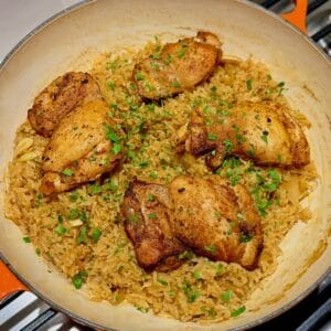 Four golden chicken thighs sit over apple cider rice with parsley.