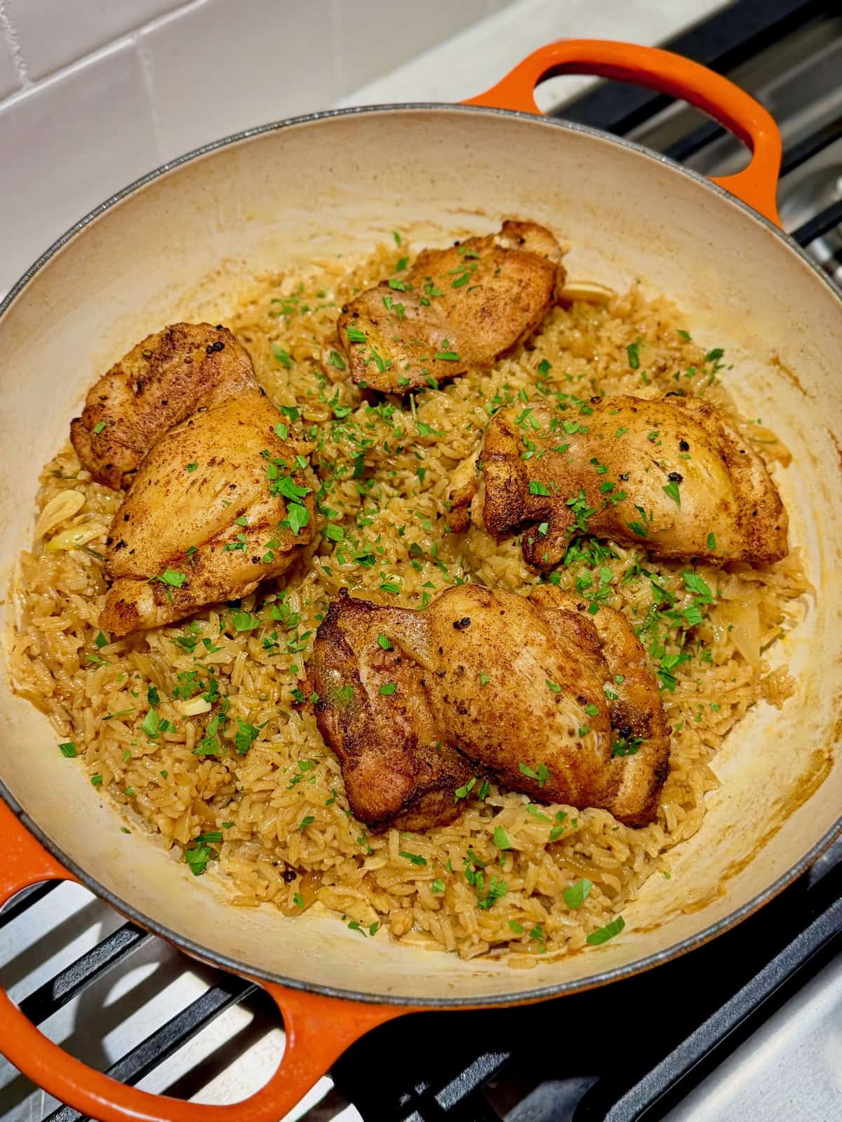 Four golden chicken thighs sit over apple cider rice with parsley.