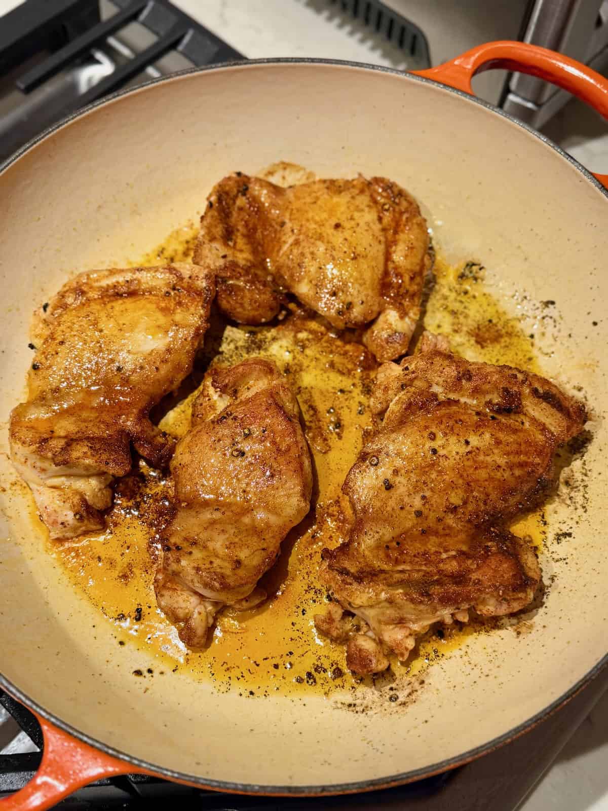 Golden brown chicken thighs seasoned with paprika sear in a braiser.